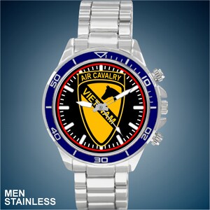 May include: A silver watch with a black face and a blue and red bezel. The face features a yellow and black emblem with the text "AIR CAVALRY VIETNAM".