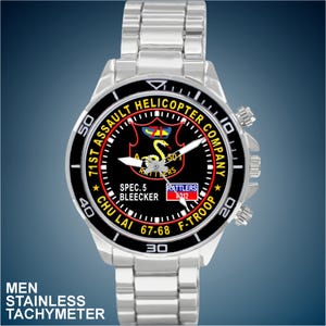 May include: Stainless steel watch with a black face featuring the text "71st Assault Helicopter Company" and "Rattlers". The watch has a silver band and a tachymeter. The watch face also includes the text "Chu Lai 67-68".