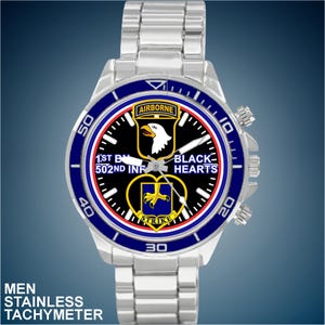 May include: A silver watch with a black face and blue bezel. The face features a military insignia with the text "AIRBORNE", "1ST BN 502ND INF", "BLACK HEARTS", and "STRIKE".