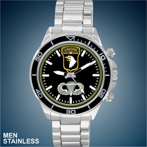 May include: A silver stainless steel wristwatch with a black face and green accents. The face features a white eagle with the word "AIRBORNE" above it and a silver parachute with wings below it. The watch has a black bezel with white numbers.