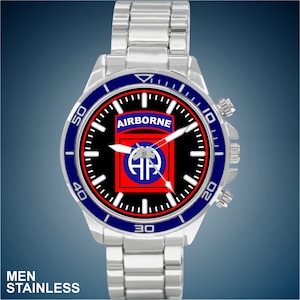 May include: A silver watch with a black face and blue bezel. The face features a red and blue emblem with the text "AIRBORNE" and a parachute symbol. The watch has a silver metal band.