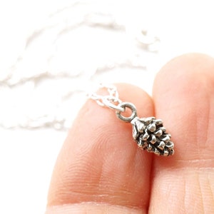 May include: A silver necklace with a small pine cone charm. The necklace is on a white background.