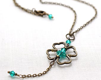 Puede incluir: Un collar de cadena de bronce con un colgante de trébol de cuatro hojas y detalles de cristal verde.