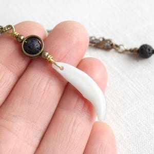 May include: A necklace featuring a white tooth pendant, a black lava rock bead, and gold-toned accents.