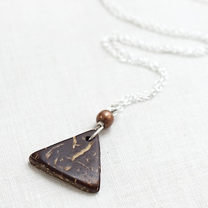 May include: A silver chain necklace with a triangular pendant made of dark brown coconut shell with gold flecks. The pendant is attached to the chain with a small copper bead.