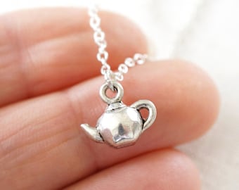 May include: A silver teapot charm necklace. The charm is small and detailed, and the chain is delicate.