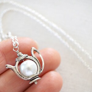 Può includere: Una collana a forma di teiera d'argento con un perla bianca all'interno. La collana è su una catena d'argento.