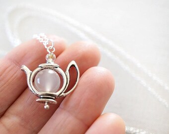 May include: A silver teapot necklace with a white gemstone in the center. The necklace is on a white chain.