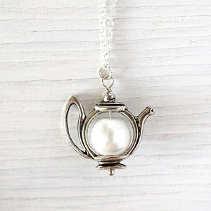 May include: A silver teapot necklace with a white pearl inside. The teapot is a charm on a silver chain.