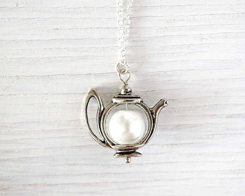 May include: A silver teapot necklace with a white pearl inside. The teapot is a charm on a silver chain.