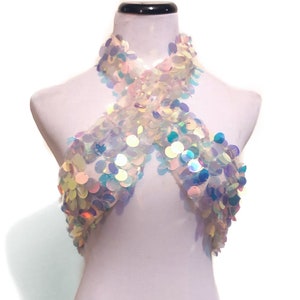 May include: A halter-style crop top covered in iridescent, circular sequins that reflect light in shades of blue, pink, and white. The garment features a crisscross neckline design and is displayed on a white mannequin torso against a plain background.