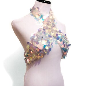 May include: A halter-style top constructed from sheer mesh fabric completely covered in iridescent, circular sequins that reflect light in various colors. The garment features a crisscross neckline design that wraps around the neck and chest area.