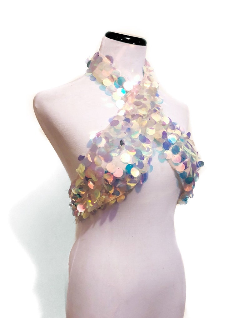 May include: A halter-style top constructed from sheer mesh fabric completely covered in iridescent, circular sequins that reflect light in various colors. The garment features a crisscross neckline design that wraps around the neck and chest area.