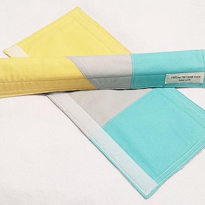 May include: A yellow, gray, and turquoise fabric armrest cushion with a white velcro strap. The cushion has a label that reads "Yellow Terrace.com Handmade".