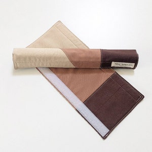 May include: A brown, beige, and tan fabric roll-up mat with a white velcro closure. The mat is made of patchwork fabric and has a label that reads "Yellow Terrace.com Handmade".