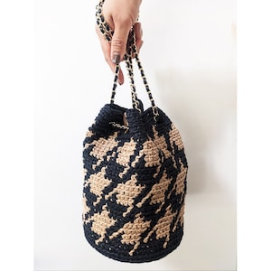 Puede incluir: Un bolso de cubo de crochet negro y marrón con una correa de cadena dorada.