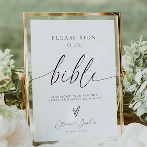 May include: A framed sign with the text "PLEASE SIGN OUR bible" in elegant script. The sign also includes the text "HIGHLIGHT YOUR FAVORITE VERSE AND WRITE US A NOTE" and the names "Olivia + Joshua" with a date. The sign is set on a wooden surface.