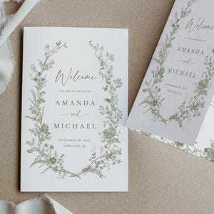May include: Wedding stationery set featuring a floral design. The set includes a flat card and a folded program, both with the names "Amanda and Michael" and the word "Welcome" in elegant script. The floral elements are in shades of green.