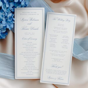 May include: Two wedding ceremony programs with blue text and borders, lying on a cream-colored satin surface. The programs are rectangular and feature the text "Welcome to the Wedding Ceremony of Lauren Robinson and Thomas Daniels." Blue hydrangeas and a blue ribbon are in the background.