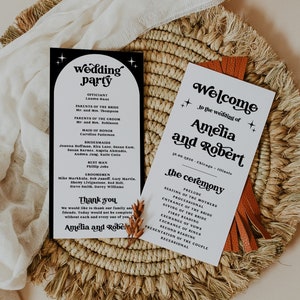 Puede incluir: Dos tarjetas de ceremonia de boda en blanco y negro con una tarjeta de fiesta de boda en blanco y negro. Las tarjetas están sobre un mantel individual de paja trenzada con una borla marrón. Las tarjetas tienen una fuente retro e incluyen los nombres Amelia y Robert.