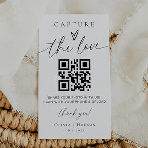 May include: A white card with the text "CAPTURE the love" and a QR code. The card also includes the text "SHARE YOUR PHOTO WITH US! SCAN WITH YOUR PHONE & UPLOAD thank you! OLIVIA • HUDSON 08.15.202X". The card is on a woven surface with white fabric.