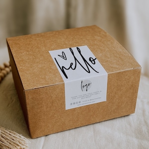 Könnte beinhalten: Ein brauner Karton mit einem weißen Etikett, auf dem "hello" mit einem Herzsymbol und dem Wort "logo" steht. Das Etikett enthält auch eine Dankesbotschaft für die Unterstützung eines kleinen Unternehmens.
