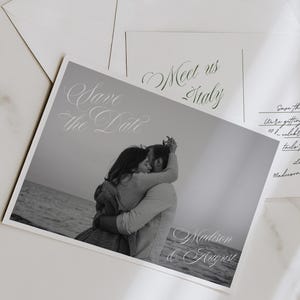 May include: A black and white Save the Date card featuring a photograph of a couple embracing by the sea, with elegant script text. The card is accompanied by a white envelope sealed with a wax stamp and a postcard with the text Meet us Italy.
