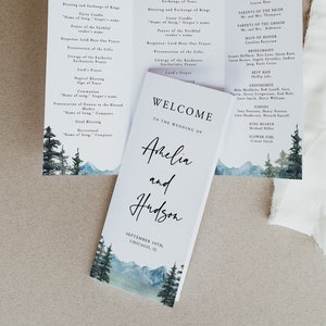 May include: Wedding ceremony programs and welcome cards. The cards feature a watercolor mountain and pine tree design. The welcome card reads "Welcome to the Wedding of Amelia and Hudson, September 19th, Chicago, IL."