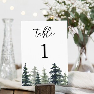 May include: White table number card with black calligraphy that reads "Table 1". The card has a watercolor illustration of a forest with green trees.