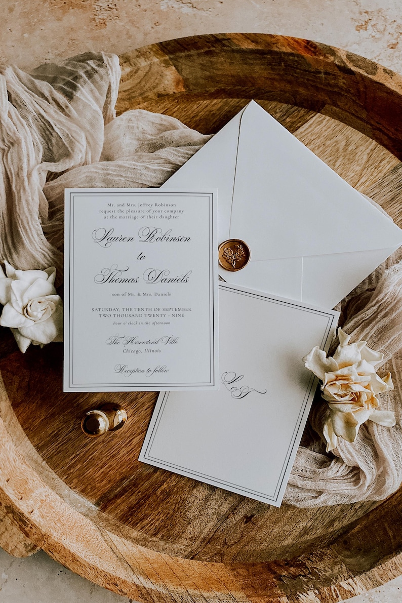 Puede incluir: Elegante conjunto de invitaciones de boda con una invitaci&oacute;n formal, una tarjeta de confirmaci&oacute;n de asistencia y un sobre con un sello de cera. La invitaci&oacute;n incluye los nombres "Lauren Robinson" y "Thomas Daniels" y los detalles del evento. El conjunto est&aacute; dispuesto sobre una bandeja de madera con detalles florales.