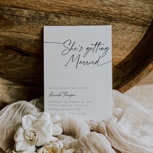 Puede incluir: Una invitaci&oacute;n de boda blanca con caligraf&iacute;a negra que dice "She's getting Married". La invitaci&oacute;n incluye el nombre de la novia, Amanda Thompson, la fecha y hora de la boda, la direcci&oacute;n y el sitio web donde los invitados pueden registrarse para regalos.