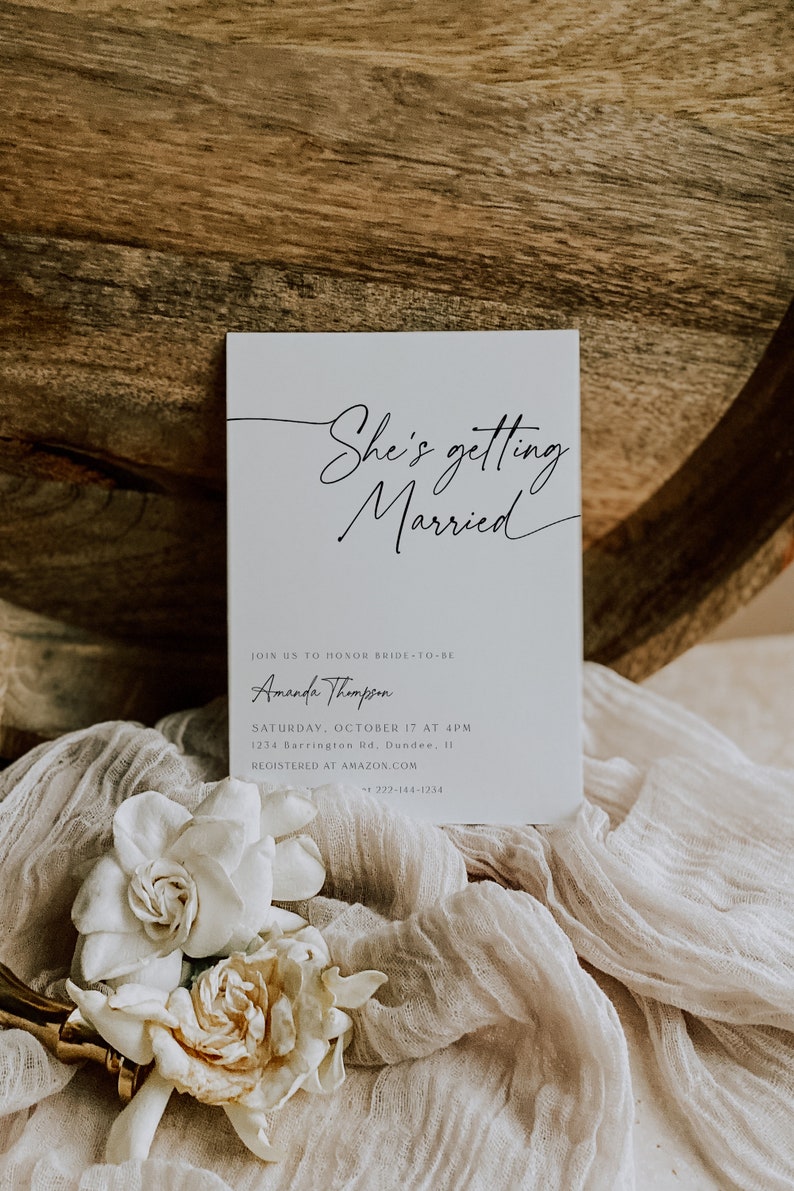 Puede incluir: Una invitaci&oacute;n de boda blanca con caligraf&iacute;a negra que dice "She's getting Married". La invitaci&oacute;n incluye el nombre de la novia, Amanda Thompson, la fecha y hora de la boda, la direcci&oacute;n y el sitio web donde los invitados pueden registrarse para regalos.