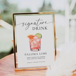 May include: A rectangular gold-toned metal frame holding a white sign that reads signature DRINK, PALOMA LIME, Tequila, Grapefruit Juice, Sparkling Water, Lemon Juice, Simple Syrup, and AMELIA + HUDSON | 8.15.20XX with a watercolor illustration of a cocktail.