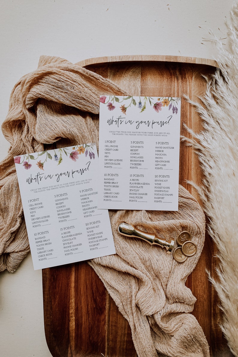 May include: Two floral-themed game cards with the title "What's in your purse?"  The cards list various items with point values assigned to each.  The cards are on a wooden surface with a beige fabric and gold wax seals.