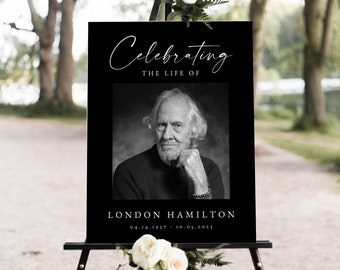 Op de afbeelding: Een zwart herdenkingsbord op een zwart schildersezel, versierd met witte bloemen. Het bord toont "Celebrating the Life of" boven een zwart-wit portret van een man. De naam "London Hamilton" en de data staan eronder.
