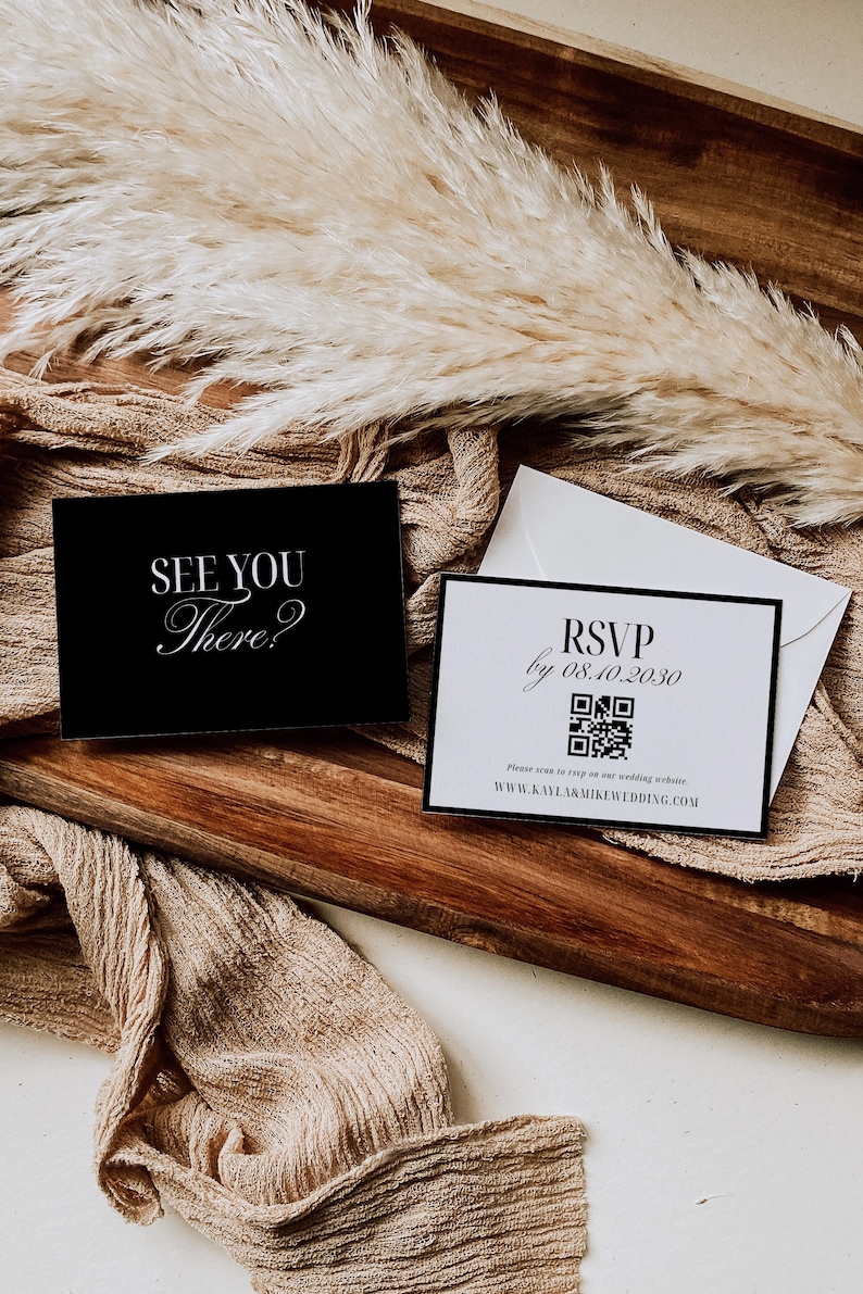 May include: Two invitation cards with text, "See You There?" and "RSVP by 08.10.2030" with a QR code, on a wooden tray. The cards are black and white with elegant fonts. Dried ornamental grass and a beige cloth are in the background.