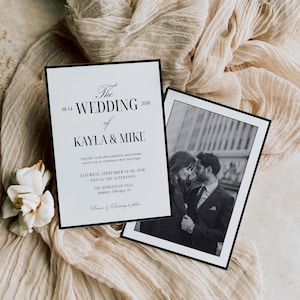 May include: Two wedding invitations with black borders rest on a beige fabric. The invitation on the left has the text "The Wedding of Kayla & Mike" and event details. The right invitation has a black and white photo of a couple.
