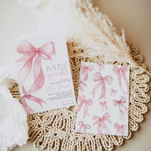 Pu&ograve; includere: Due inviti per baby shower con fiocchi rosa ad acquerello. Un invito recita "BABY sprinkle" e include i dettagli dell'evento. La seconda carta presenta un motivo di fiocchi rosa. Le carte sono su un sottobicchiere intrecciato con elementi decorativi.
