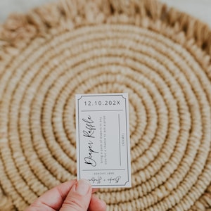 May include: A white ticket with black text for a diaper raffle. The text reads "Diaper Raffle" and "bring a pack of diapers in any size for a chance to win a prize". The date "12.10.202X" is printed at the top of the ticket.