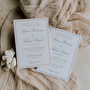 Puede incluir: Dos invitaciones de boda con caligraf&iacute;a elegante, una con borde y texto burdeos, la otra con borde azul. Las invitaciones est&aacute;n sobre una tela beige con una flor blanca. El texto dice "Lauren Robinson a Thomas Daniels".