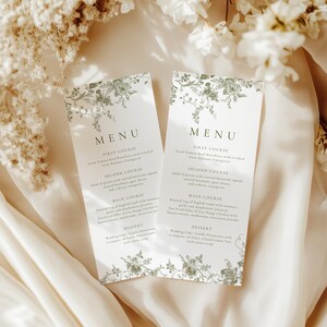 Puede incluir: Dos tarjetas de men&uacute; blancas con un dise&ntilde;o floral verde. La palabra "MENU" est&aacute; en la parte superior, con descripciones de los platos debajo. Las tarjetas est&aacute;n sobre una tela color crema, con flores blancas en el fondo.