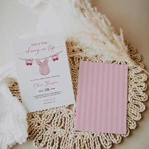May include: A baby shower invitation with the text "She's the cherry on top" and a pink onesie graphic. The invitation includes details for Olivia Thompson's baby shower on August 28th at 2 PM. A pink striped card is next to the invitation.