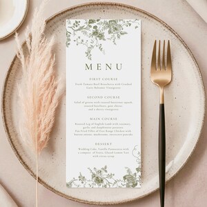 Puede incluir: Una tarjeta de men&uacute; con un dise&ntilde;o floral verde, que presenta los platos de una comida. La tarjeta est&aacute; sobre un plato beige con un tenedor dorado y negro. Hierba ornamental seca a la izquierda.