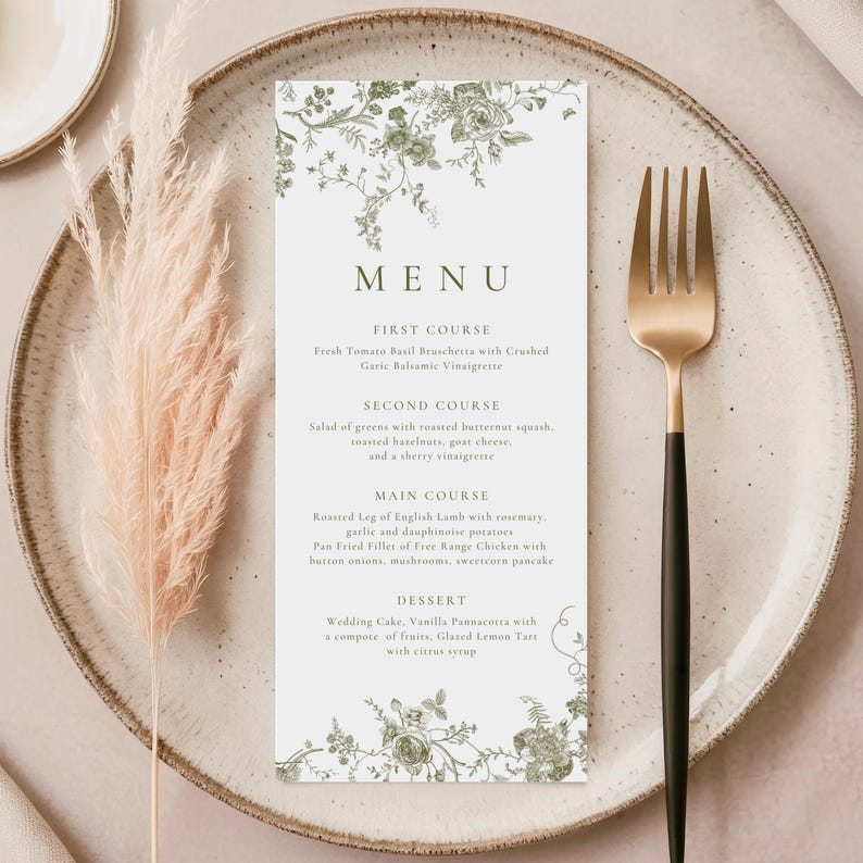 Puede incluir: Una tarjeta de men&uacute; con un dise&ntilde;o floral verde, que presenta los platos de una comida. La tarjeta est&aacute; sobre un plato beige con un tenedor dorado y negro. Hierba ornamental seca a la izquierda.