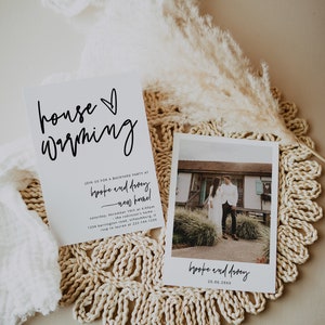 May include: A white card with black calligraphy that reads "house warming" and an invitation to a backyard party for Brooke and Dacey at their new home on December 10th at 4:00pm. The address is 1234 Barrington Road, Schaumburg, IL. RSVP to Lauren at 222-144-1234. A Polaroid photo of Brooke and Dacey standing in front of their new home is on the right side of the card.
