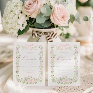 K&ouml;nnte beinhalten: Zwei Einladungskarten mit Blumen- und Schleifendesigns. Die Karten tragen die Aufschrift "Olivia's FIRST BIRTHDAY" mit dem Datum 20. August um 16:00 Uhr. Eine Vase mit einer gestreiften Schleife enth&auml;lt einen Strau&szlig; aus rosa Rosen, wei&szlig;en Hortensien und Gr&uuml;n.