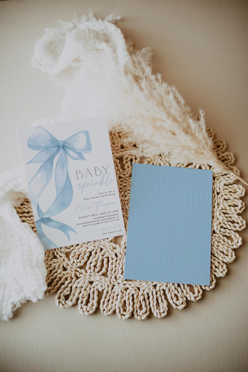 May include: A baby shower invitation with a light blue bow illustration and the words "BABY sprinkle". A light blue card is next to the invitation. The invitation includes the date, time, and location.