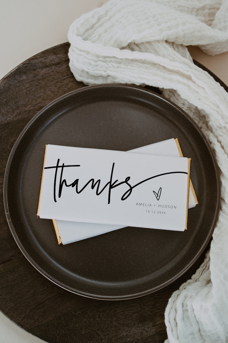 Peut inclure: Barre de chocolat blanc envelopp&eacute;e de papier d'or. La barre comporte un texte noir qui dit "Merci" avec un symbole de c&oelig;ur et les noms "Amelia + Hudson" et la date "10-12-20XX".