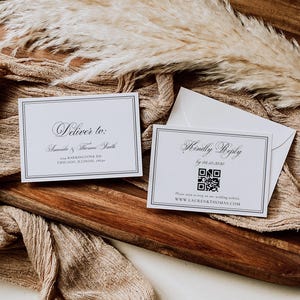 Puede incluir: Dos tarjetas de invitaci&oacute;n de boda blancas con texto negro y borde negro, una con la leyenda "Deliver to:" y la otra "Kindly Reply". Un c&oacute;digo QR est&aacute; en la segunda tarjeta. Las tarjetas est&aacute;n sobre una bandeja de madera con tela beige y plantas secas.