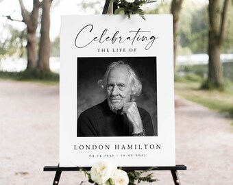 Könnte beinhalten: Ein weißes Schild mit schwarzem Text, auf dem steht "Celebrating the Life of London Hamilton 04.14.1937 - 10.05.2021". Ein Schwarzweißfoto eines Mannes befindet sich in der Mitte des Schildes. Das Schild steht auf einem schwarzen Staffelei.